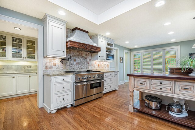 kitchen featuring premium range hood, appliances with stainless steel finishes, white cabinets, and light hardwood / wood-style floors