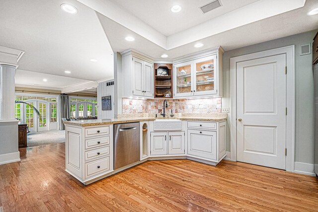 kitchen with white cabinets, tasteful backsplash, stainless steel dishwasher, decorative columns, and light hardwood / wood-style flooring