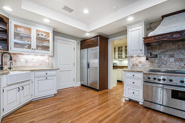 kitchen with decorative backsplash, white cabinets, custom range hood, light hardwood / wood-style floors, and high end appliances