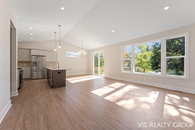 unfurnished living room with lofted ceiling, sink, light hardwood / wood-style flooring, and a notable chandelier