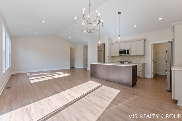 kitchen with a center island with sink, appliances with stainless steel finishes, vaulted ceiling, light hardwood / wood-style flooring, and decorative light fixtures