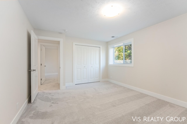 unfurnished bedroom featuring light carpet, a closet, and a textured ceiling