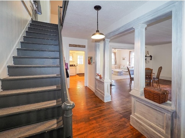 staircase featuring ornate columns, hardwood / wood-style flooring, and a textured ceiling