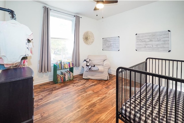 bedroom with hardwood / wood-style flooring, a crib, and ceiling fan