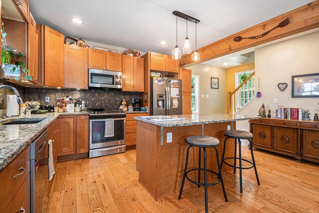 kitchen with light stone countertops, appliances with stainless steel finishes, sink, and light wood-type flooring