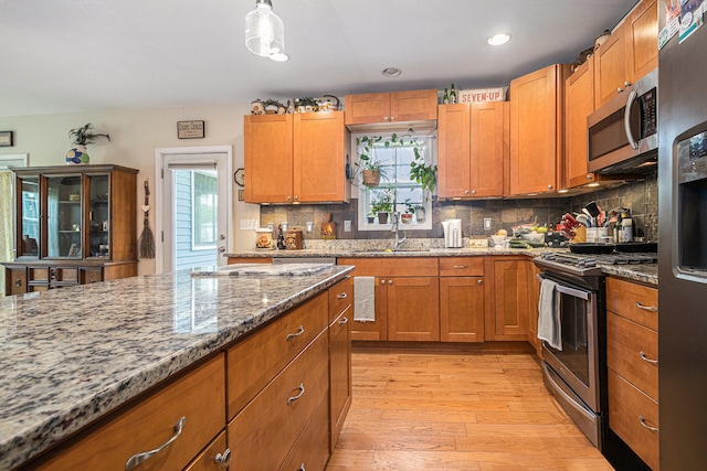 kitchen with decorative backsplash, appliances with stainless steel finishes, light hardwood / wood-style flooring, sink, and light stone counters