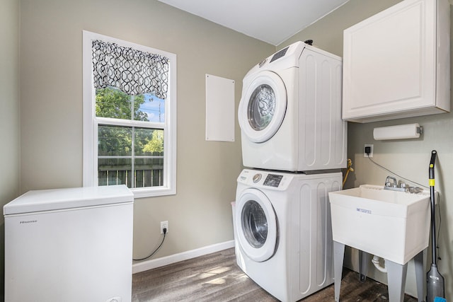 laundry area featuring dark hardwood / wood-style flooring, stacked washer and dryer, and cabinets