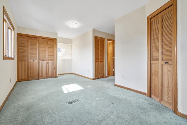 unfurnished bedroom featuring light carpet and two closets