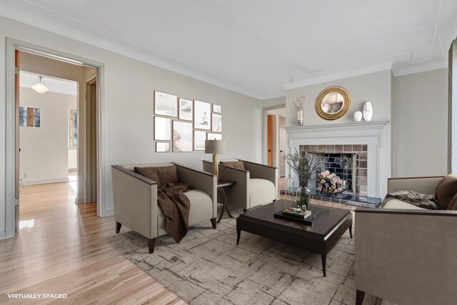 living room featuring light hardwood / wood-style flooring, crown molding, and a tiled fireplace