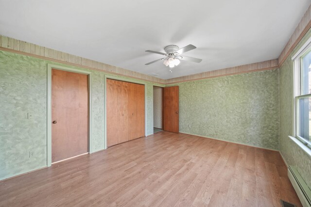 unfurnished bedroom with light hardwood / wood-style flooring, ceiling fan, a baseboard heating unit, and two closets