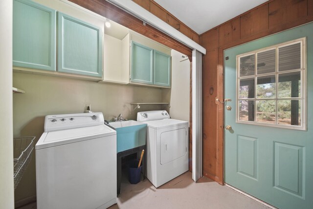 laundry area with sink, wood walls, cabinets, and separate washer and dryer