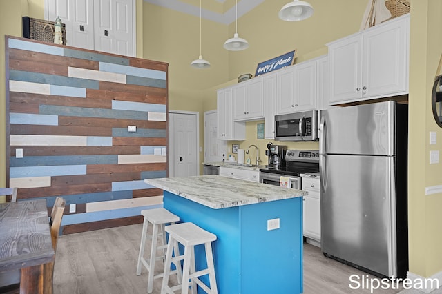 kitchen with stainless steel appliances, decorative light fixtures, a center island, light hardwood / wood-style floors, and white cabinetry