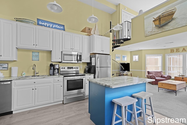 kitchen with white cabinetry, hanging light fixtures, stainless steel appliances, and light wood-type flooring