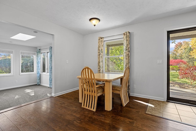 dining space featuring a skylight, a textured ceiling, a healthy amount of sunlight, and dark hardwood / wood-style flooring