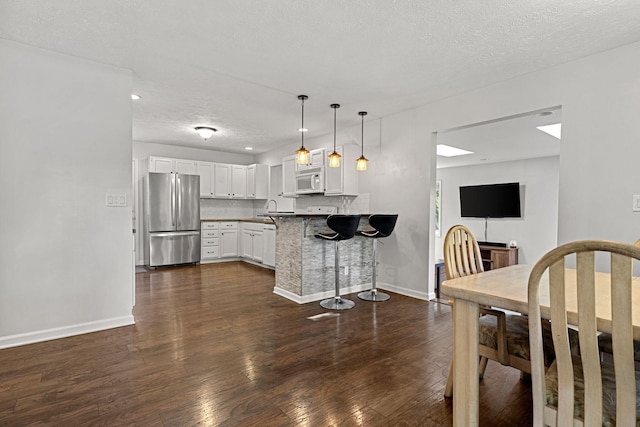 kitchen with kitchen peninsula, stainless steel fridge, a kitchen bar, pendant lighting, and white cabinetry