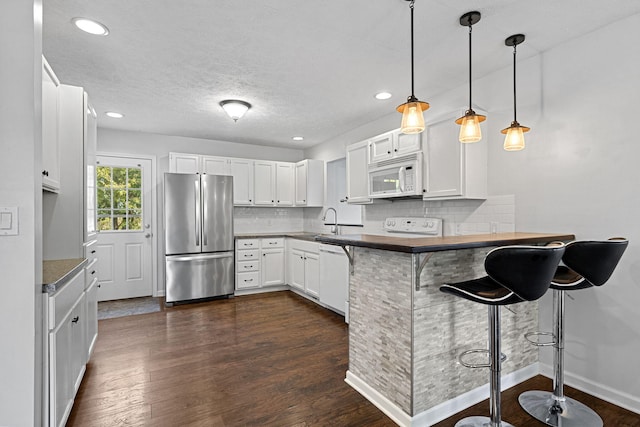 kitchen featuring a kitchen breakfast bar, white cabinetry, dark wood-type flooring, and white appliances