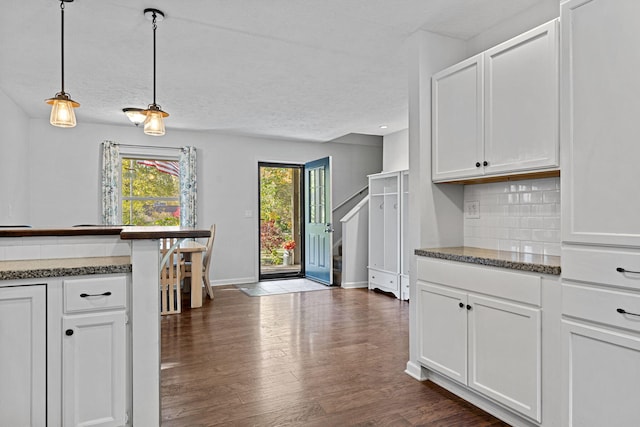 kitchen with dark hardwood / wood-style floors, backsplash, dark stone countertops, pendant lighting, and white cabinets