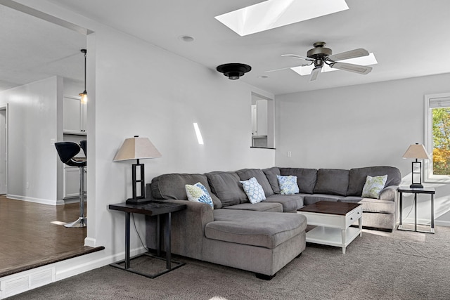 living room featuring ceiling fan, a skylight, and dark carpet