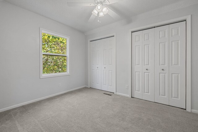 unfurnished bedroom with multiple closets, light carpet, a textured ceiling, and ceiling fan