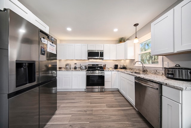 kitchen featuring appliances with stainless steel finishes, sink, light wood-type flooring, white cabinetry, and pendant lighting