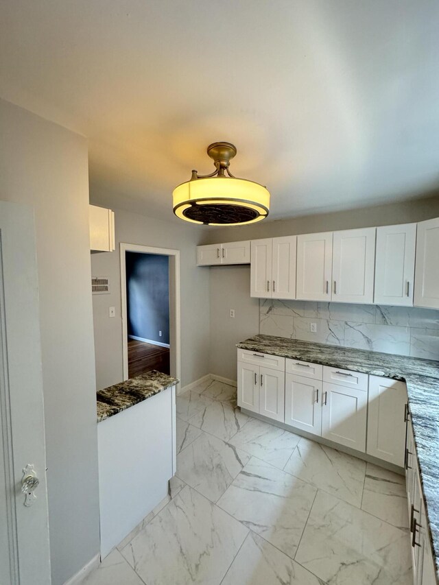 kitchen featuring decorative backsplash, white cabinetry, and dark stone countertops