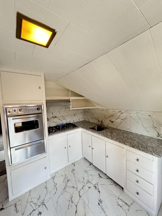 kitchen with gas stovetop, lofted ceiling, oven, backsplash, and white cabinets