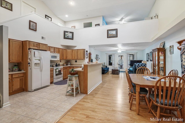 kitchen with light hardwood / wood-style floors, a kitchen breakfast bar, ceiling fan, white appliances, and a high ceiling