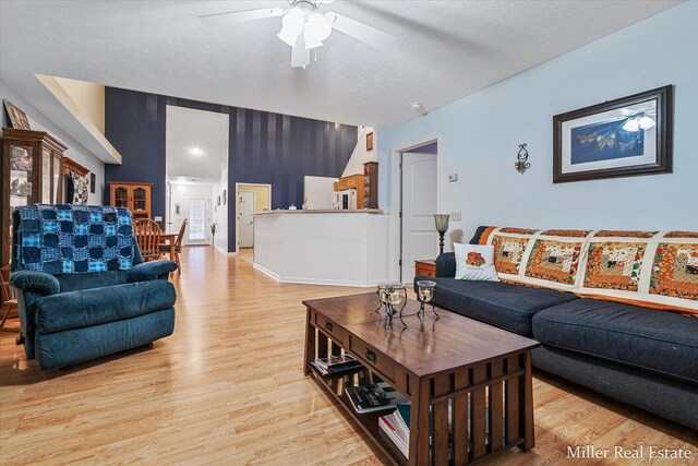 living room with a textured ceiling, light wood-type flooring, and ceiling fan