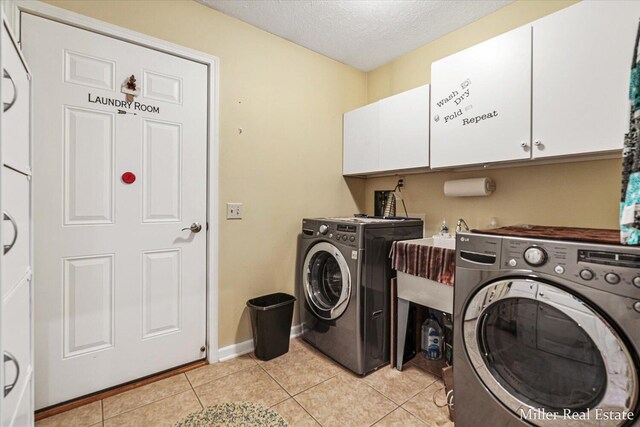 laundry room with a textured ceiling, washer and clothes dryer, cabinets, and light tile patterned floors