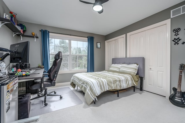 bedroom with multiple closets, light colored carpet, and ceiling fan