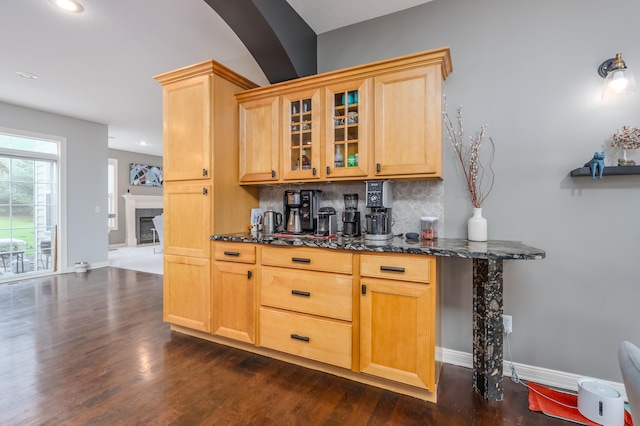 bar featuring decorative backsplash, dark stone countertops, light brown cabinetry, and dark hardwood / wood-style floors