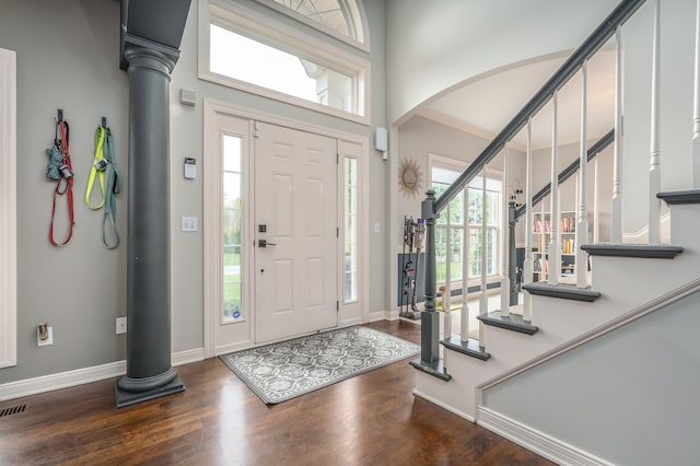 foyer featuring dark wood-type flooring, decorative columns, and a high ceiling