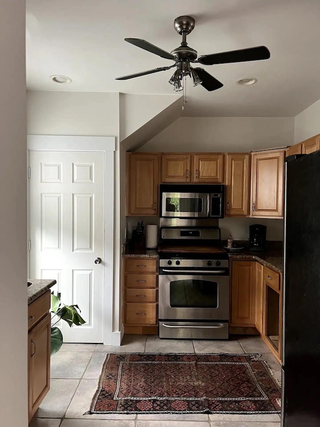 kitchen with dark stone countertops, stainless steel appliances, light tile patterned floors, and ceiling fan