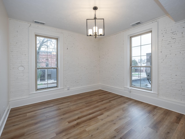 spare room with hardwood / wood-style floors, a notable chandelier, and brick wall