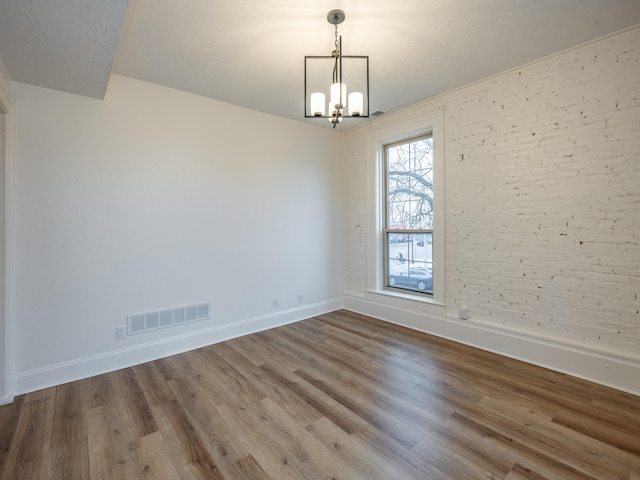 spare room featuring a textured ceiling, a chandelier, wood-type flooring, and brick wall