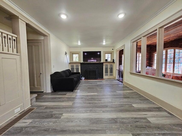 living room featuring dark wood-type flooring, crown molding, and a brick fireplace