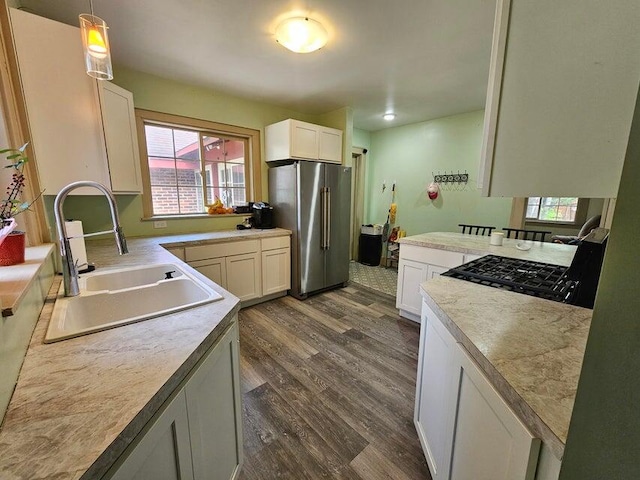 kitchen with sink, hanging light fixtures, stainless steel fridge, white cabinets, and dark wood-type flooring