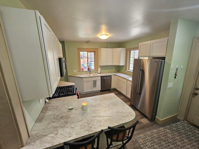 kitchen featuring kitchen peninsula, white cabinets, appliances with stainless steel finishes, a kitchen breakfast bar, and dark wood-type flooring