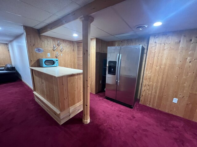 bar with wood walls, stainless steel fridge, dark colored carpet, and a paneled ceiling