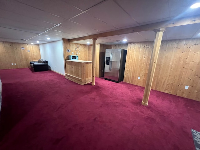 basement featuring carpet, wood walls, and stainless steel fridge with ice dispenser