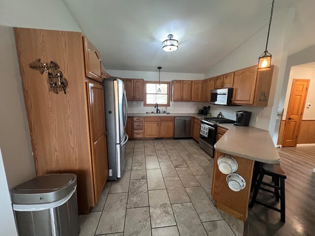 kitchen featuring stainless steel appliances, sink, a kitchen bar, hanging light fixtures, and vaulted ceiling