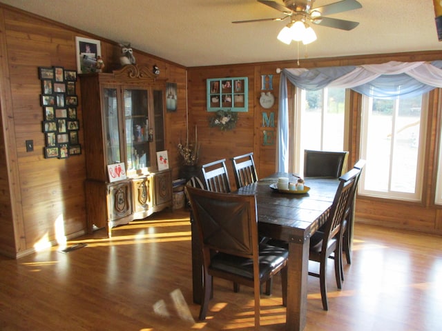 dining room with wooden walls, hardwood / wood-style flooring, ceiling fan, and lofted ceiling