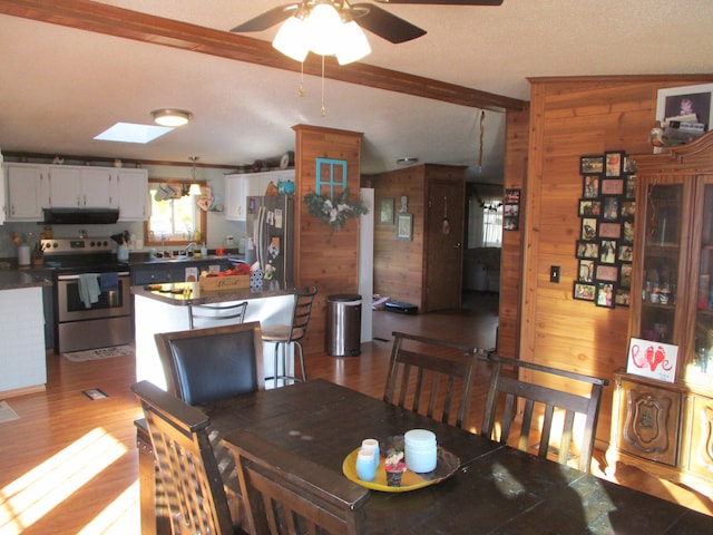 dining area featuring light hardwood / wood-style floors, lofted ceiling with skylight, ceiling fan, and wooden walls