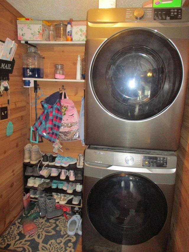 washroom with stacked washer / drying machine and wood walls