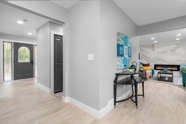 foyer entrance with a high end fireplace and light wood-type flooring