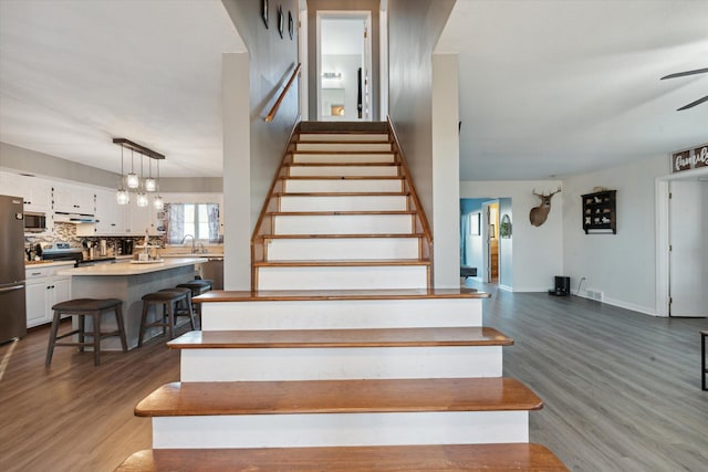 staircase featuring ceiling fan, hardwood / wood-style flooring, and sink