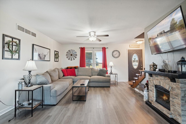 living room featuring a stone fireplace, light hardwood / wood-style floors, and ceiling fan