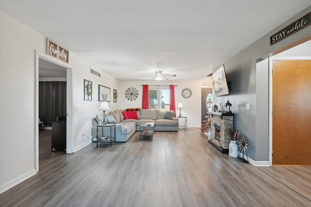 living room with a stone fireplace, wood-type flooring, and ceiling fan