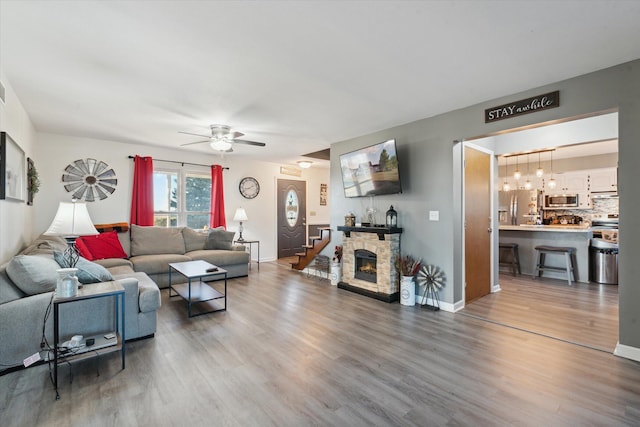 living room featuring a stone fireplace, wood-type flooring, and ceiling fan