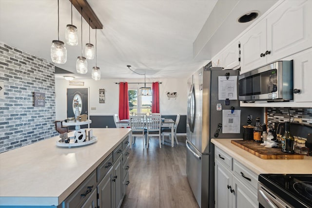 kitchen with decorative backsplash, appliances with stainless steel finishes, white cabinetry, dark wood-type flooring, and decorative light fixtures